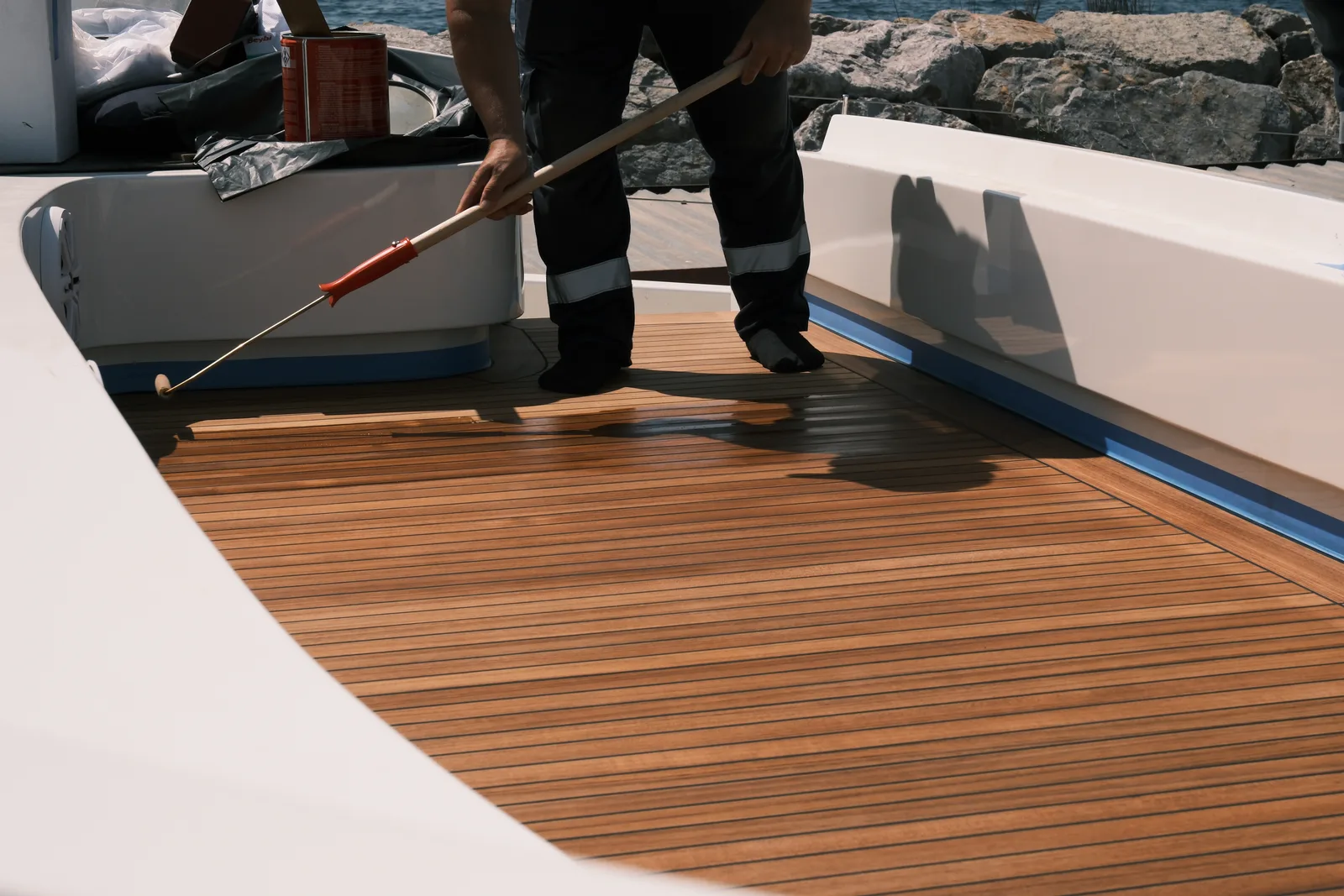 TECHNICIAN FINISHING A NEWLY LAID TEAK DECK ON A YACHT'S AFT DECK